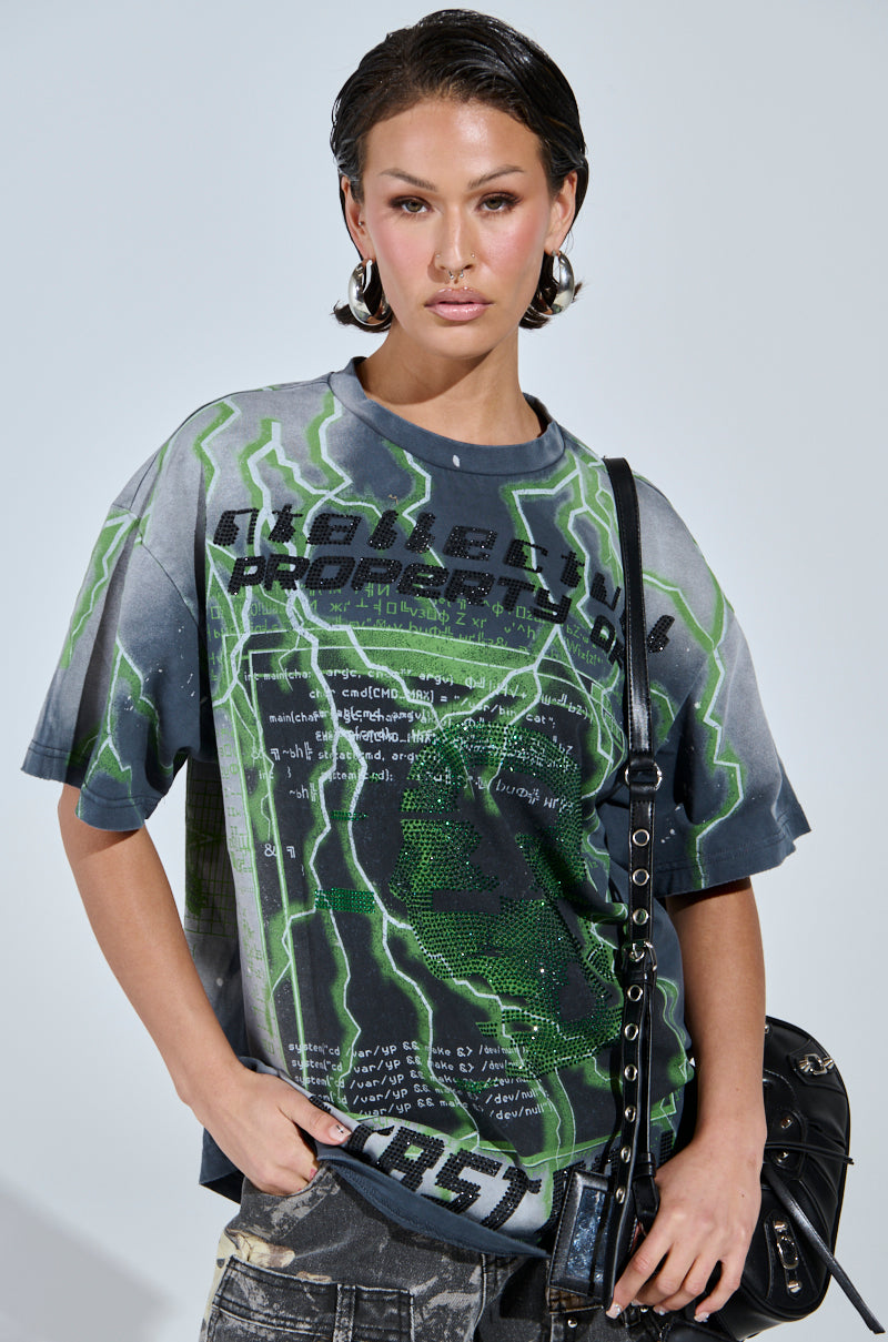 With wet-styled hair, a person confidently poses in the FIRST ONE HERE OVERSIZED GRAPHIC TEE, showcasing a green lightning design and bold text. Crafted from 100% cotton, they carry a black bag and wear faded denim pants against a simple, light background.