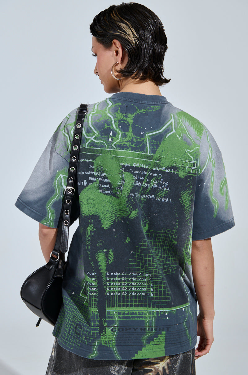 A person with short hair and a side shave is turned away, wearing the FIRST ONE HERE OVERSIZED GRAPHIC TEE, featuring futuristic graphic prints and text. They carry a black shoulder bag with silver studs against a plain off-white background.