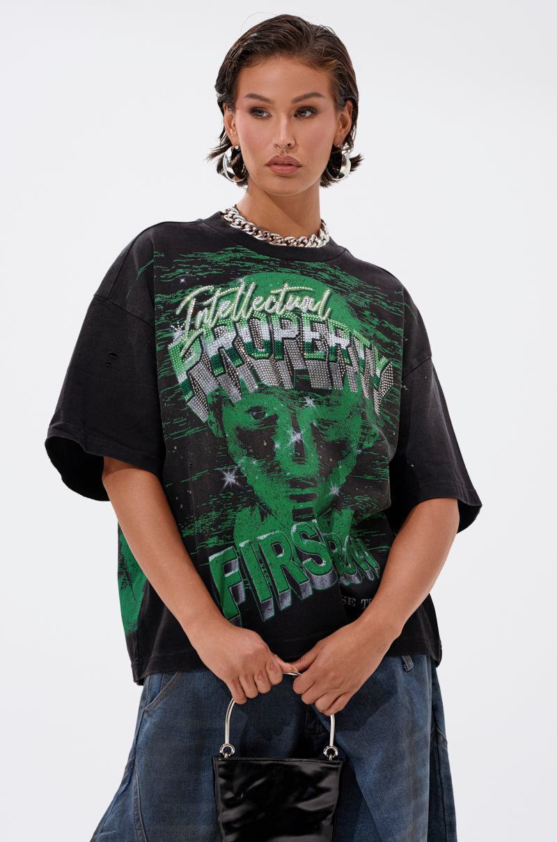 A person with short, slicked-back hair wears the PROPERTY OVERSIZED GRAPHIC TEE in black, featuring a green graphic and "Intellectual Property First" text. They accessorize with a chunky chain necklace and carry a small black handbag.