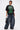 A woman poses in the PROPERTY OVERSIZED GRAPHIC TEE with green lettering, paired with wide-leg blue jeans, chunky shoes, a shiny black handbag, chain necklace, and slicked-back short hair.