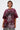 A person with short, wavy hair wears the INTELLECTUAL PROPERTY GRAPHIC TEE IN BURGUNDY, featuring bold graphics and a warning motif, paired with a leopard print skirt.