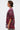 A person with short dark hair and large hoop earrings wears the INTELLECTUAL PROPERTY GRAPHIC TEE IN BURGUNDY and leopard print pants, standing in profile against a plain light background.