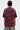 A person with short brown hair, seen from behind, wears the INTELLECTUAL PROPERTY GRAPHIC TEE IN BURGUNDY featuring bold warning text and copyright symbols, paired with leopard print pants against a plain light background.