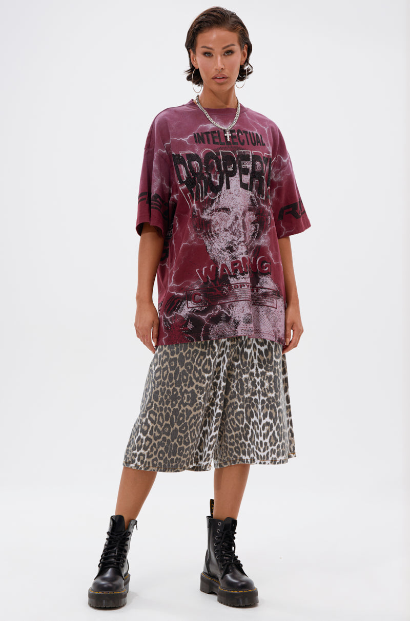 A woman stands against a plain white background wearing the INTELLECTUAL PROPERTY GRAPHIC TEE IN BURGUNDY, paired with a gray leopard-print skirt and black lace-up combat boots.