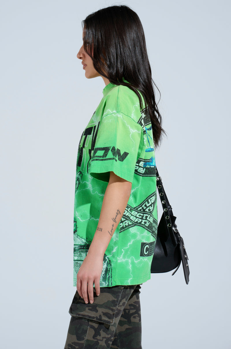 A person in an oversized silhouette is wearing a bright green INTELLECTUAL PROPERTY GRAPHIC TEE featuring eye-catching abstract graphics on a light background, with camo pants and holding a black crossbody bag.