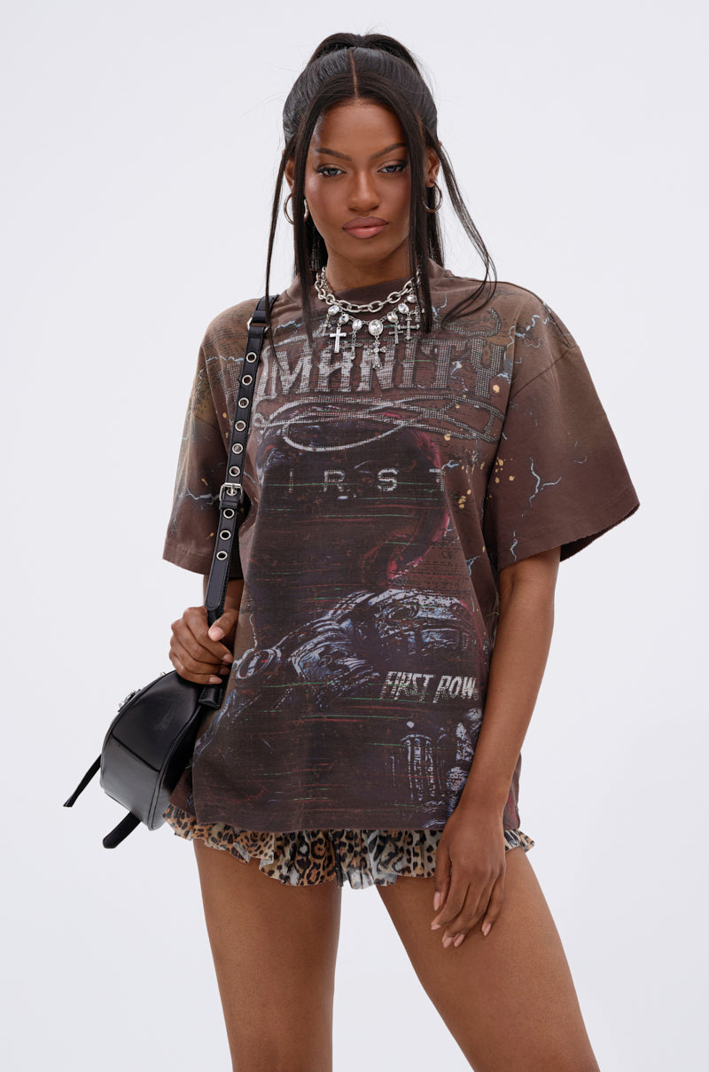A woman with long dark hair in a high half-up ponytail wears the HUMANITY OVERSIZED GRAPHIC TEE, leopard print shorts, a chunky chain necklace, and holds a small black crossbody bag while standing against a plain white background. 0