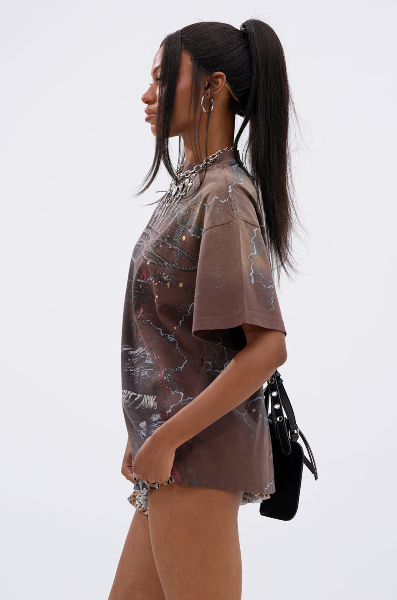A woman with long, straight black hair in a high ponytail wears the HUMANITY OVERSIZED GRAPHIC TEE, patterned shorts, hoop earrings, and carries a black shoulder bag. She stands in profile against a plain light background. 3