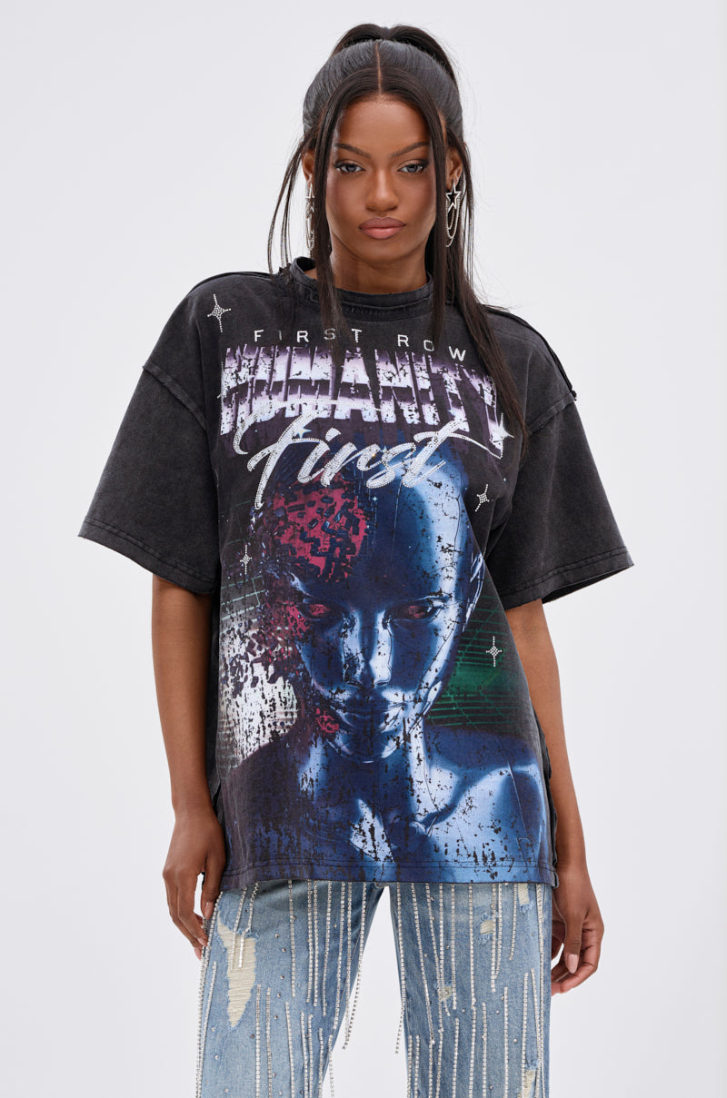 A woman with long dark hair wears the OUT OF BODY OVERSIZED GRAPHIC TEE, featuring a futuristic blue female figure and metallic text, paired with distressed, paint-splattered jeans against a plain light gray background. 0