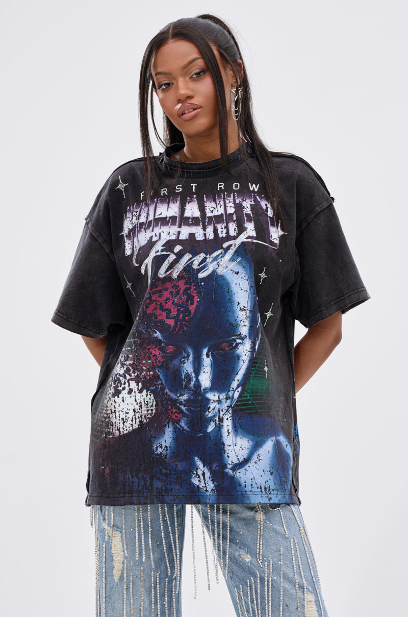 A woman with long dark hair wears the OUT OF BODY OVERSIZED GRAPHIC TEE with abstract text and a futuristic face, paired with ripped acid-wash jeans and silver chains, standing against a plain light background. 2