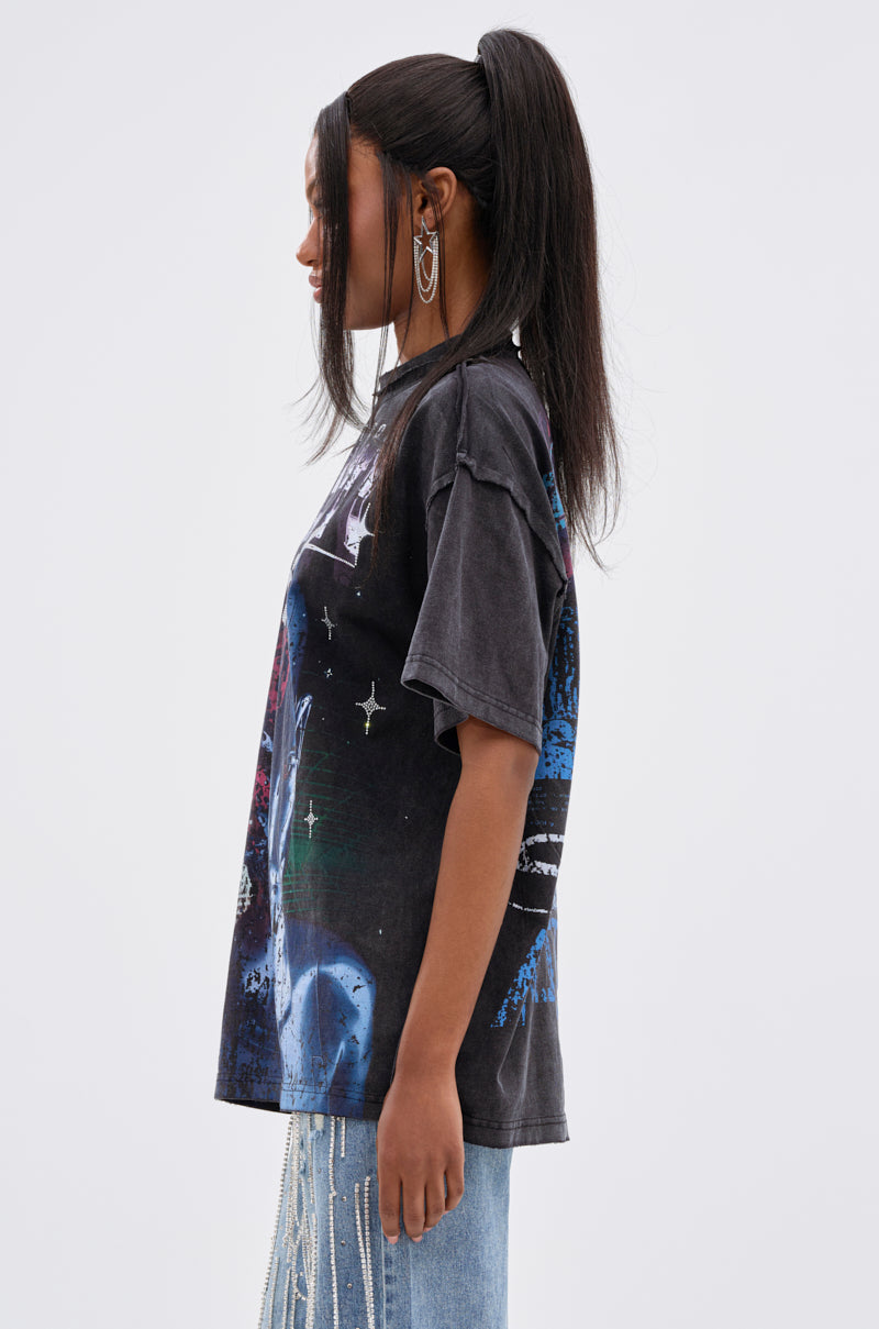 A woman with long dark hair in a high ponytail stands in profile against a white background, wearing the OUT OF BODY OVERSIZED GRAPHIC TEE styled with light blue jeans and chains for a streetwear-inspired look. 3