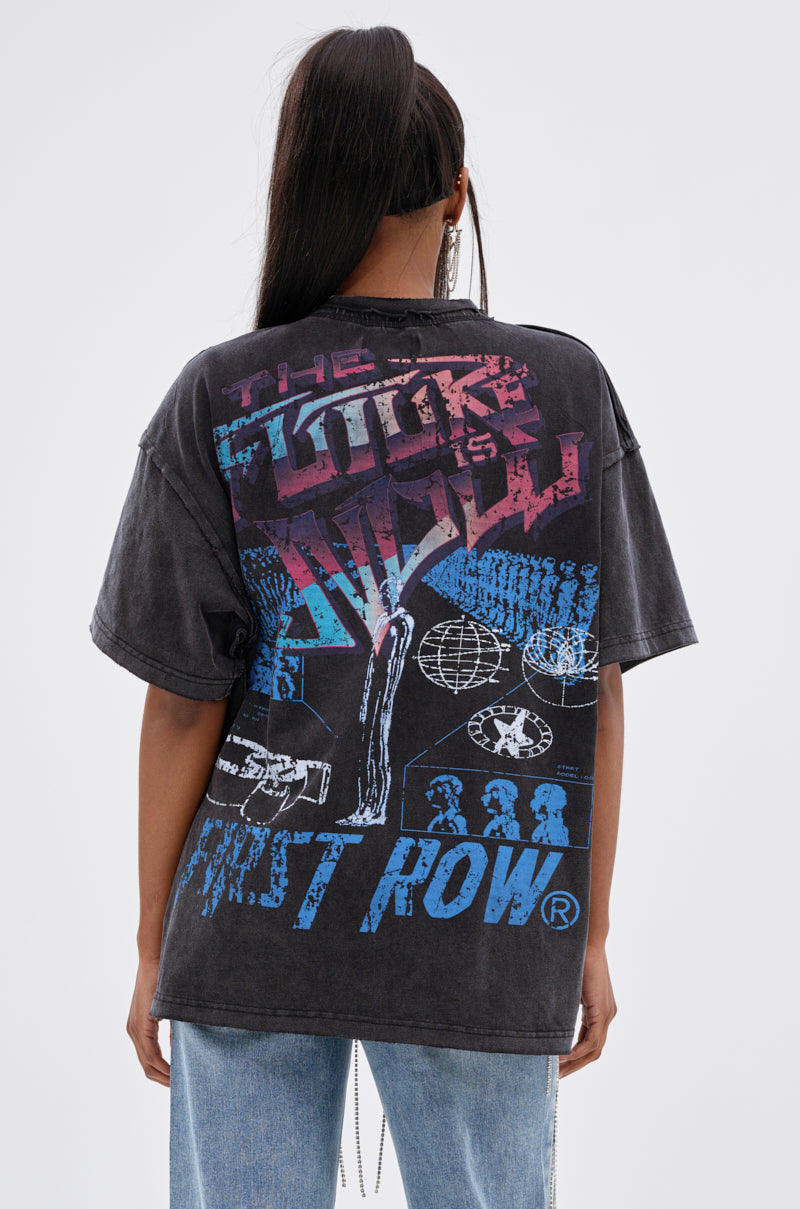 A person with long dark hair is seen from behind wearing the OUT OF BODY OVERSIZED GRAPHIC TEE, a faded black streetwear piece featuring colorful abstract graphics and bold "THE FUTURE IS" and "FIRST ROW®" text on the back. 4