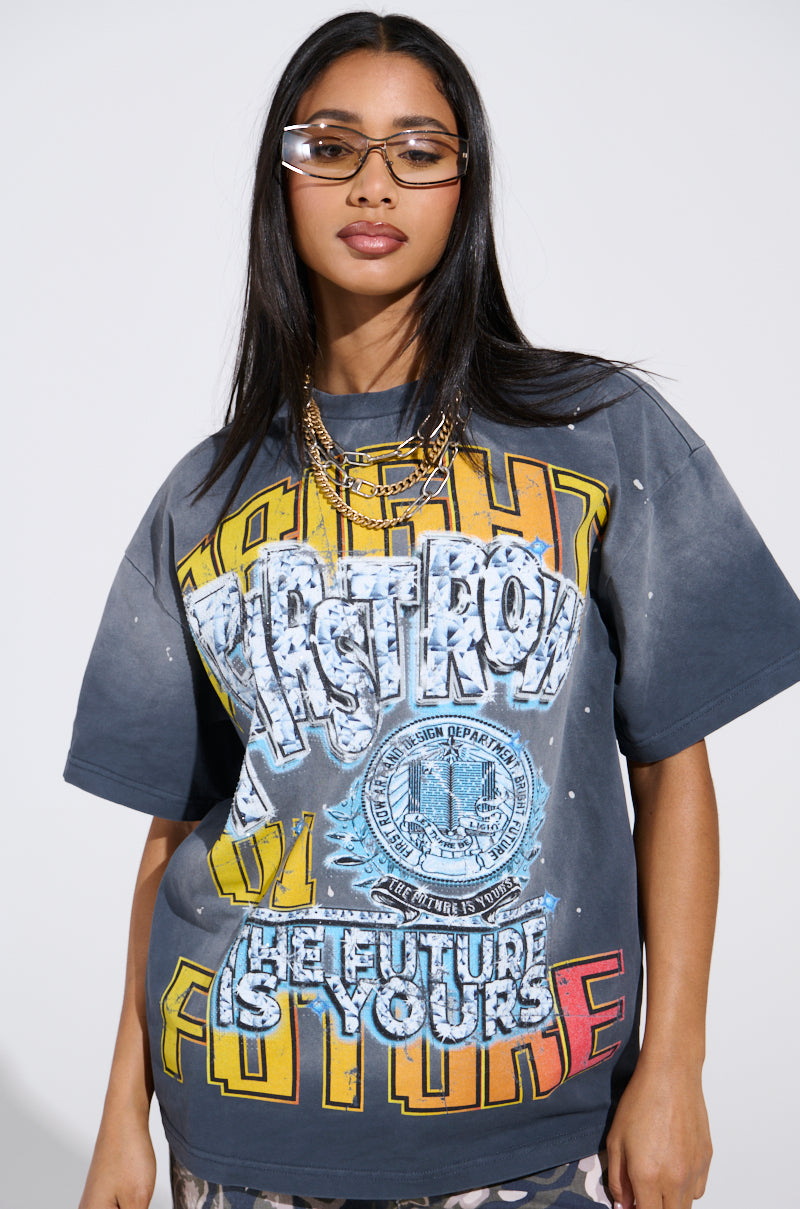 With confidence, a person wears oversized sunglasses and layered gold necklaces, showcasing THE FUTURE IS YOURS OVERSIZED GRAPHIC TEE. This tee features rhinestone embellishments with text "PASTORAL" and colorful art, making a bold statement.