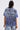 A person with long dark hair stands facing away, wearing the IRREVERENT OVERSIZED GRAPHIC TEE with bold black lettering and a lightning graphic on the back, paired with patchwork denim jeans.