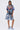 A person stands facing forward in the IRREVERENT OVERSIZED GRAPHIC TEE, paired with patchwork denim shorts featuring star designs and fluffy light blue slippers, set against a plain white background.