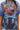 Person wears the IRREVERENT OVERSIZED GRAPHIC TEE, which showcases a large red planet, abstract blue and black patterns, distressed paint splatters, and bold yellow and red text. A silver necklace is partially visible.