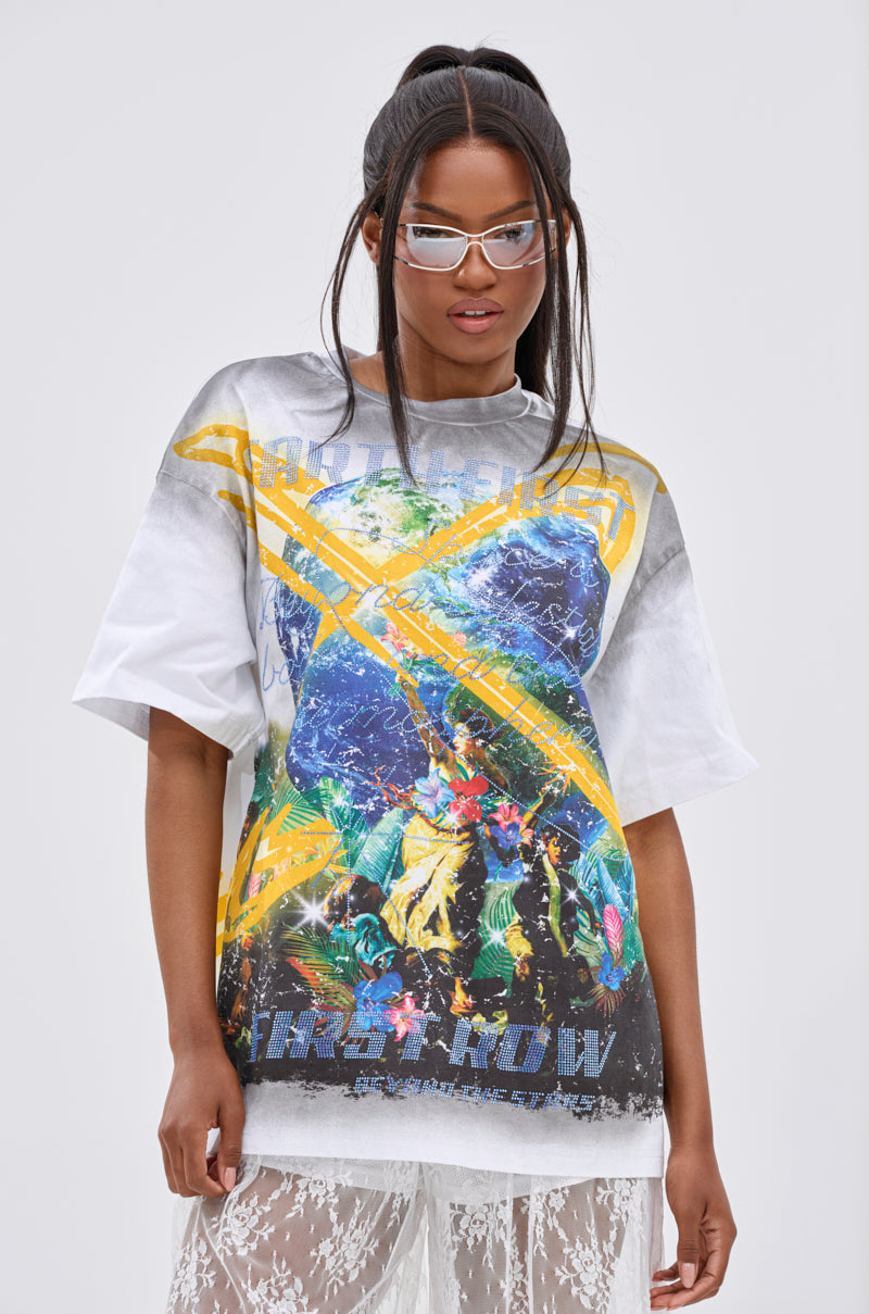 A woman wearing the NEW WORLD OVERSIZED GRAPHIC TEE and sheer lace pants stands against a plain light background, confidently looking at the camera through her clear glasses.