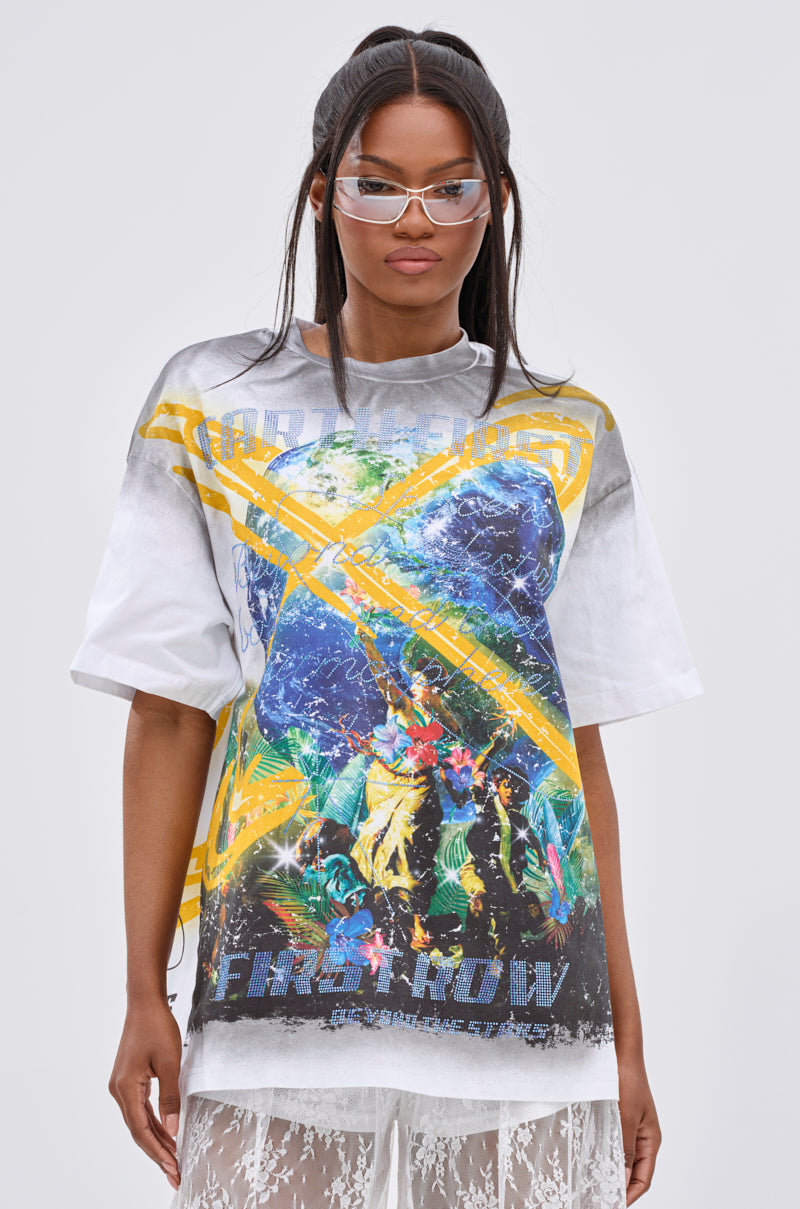 A woman with long dark hair and clear glasses stands against a gray background, wearing the NEW WORLD OVERSIZED GRAPHIC TEE with planetary and figure motifs, styled streetwear over a white lace skirt.