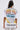 A person with long hair faces away, wearing the NEW WORLD OVERSIZED GRAPHIC TEE with colorful text, yellow accents, a planetary motif, and bold cursive streetwear style featuring "FIRST ROW" and "BEYOND THE STARS.