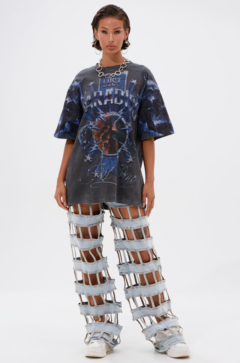 A woman wears the INSANE OVERSIZED TEE with light denim pants featuring horizontal strap cutouts. She completes her outfit with chunky sneakers and a statement necklace, standing against a plain white background.