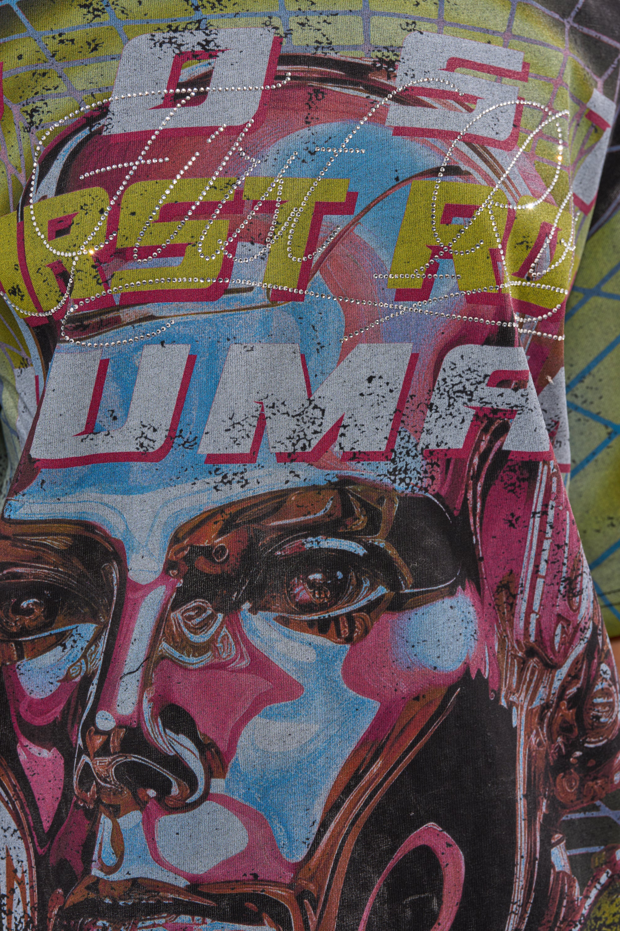 Close-up of the FIRST ROW NEW METAVERSE OVERSIZED GRAPHIC TEE featuring a vibrant cyber design with a stylized robotic face, bold layered text, and grid pattern in pink, blue, yellow, and metallic details for standout streetwear style. 6