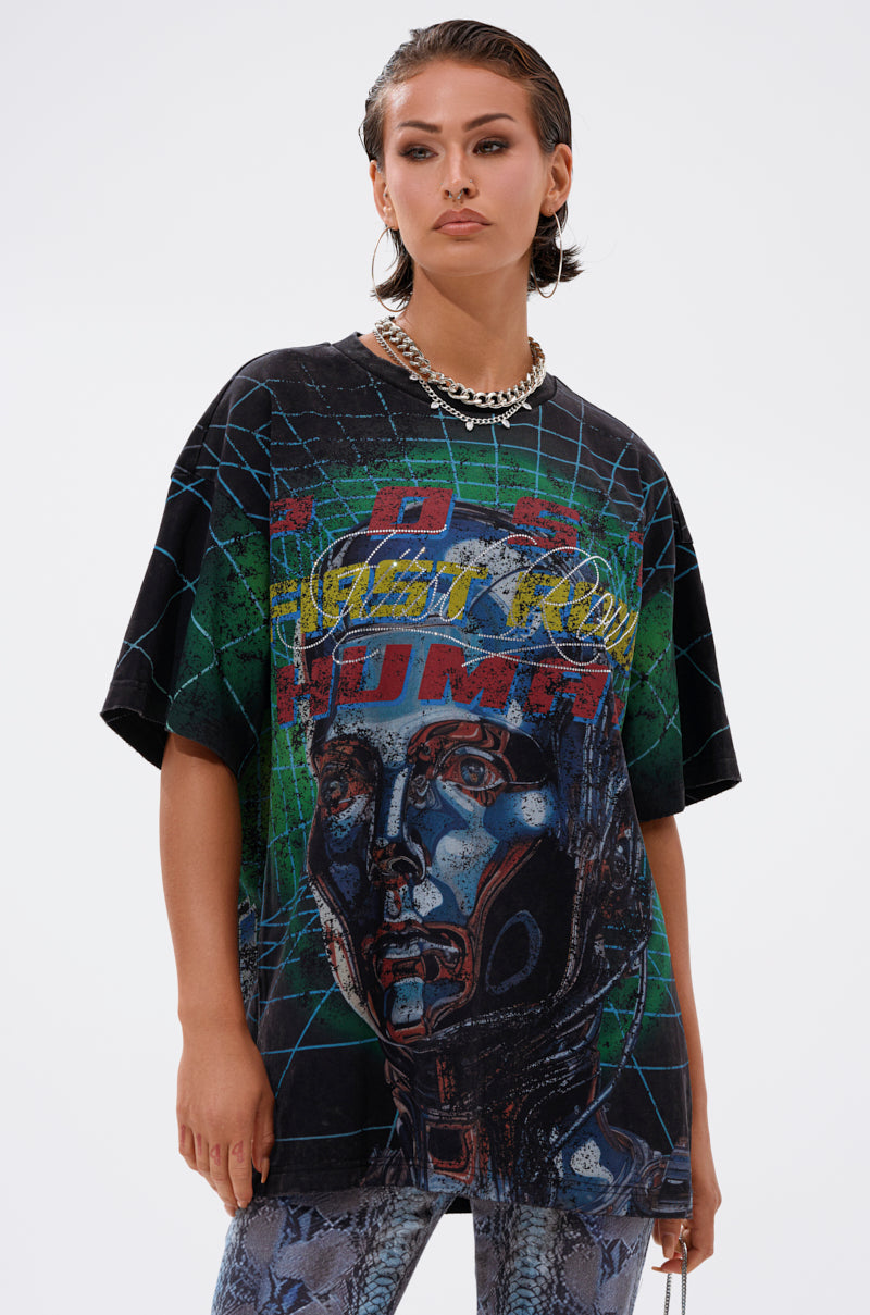 A person with slicked-back hair wears the METAVERSE OVERSIZED GRAPHIC TEE featuring a robotic face, geometric designs, and colorful text, styled with a chunky chain necklace and patterned pants against a white background.