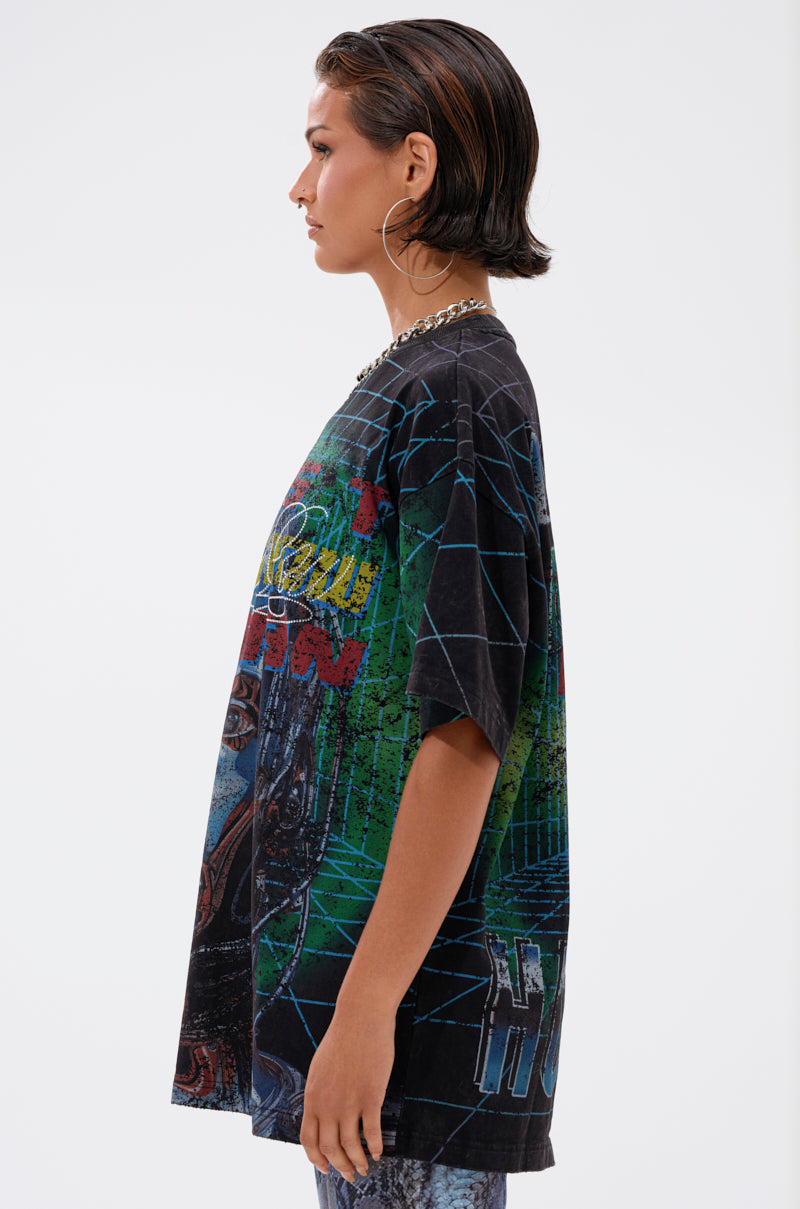 A person with short dark hair, hoop earrings, and a chain necklace models the METAVERSE OVERSIZED GRAPHIC TEE in profile against a plain white background.