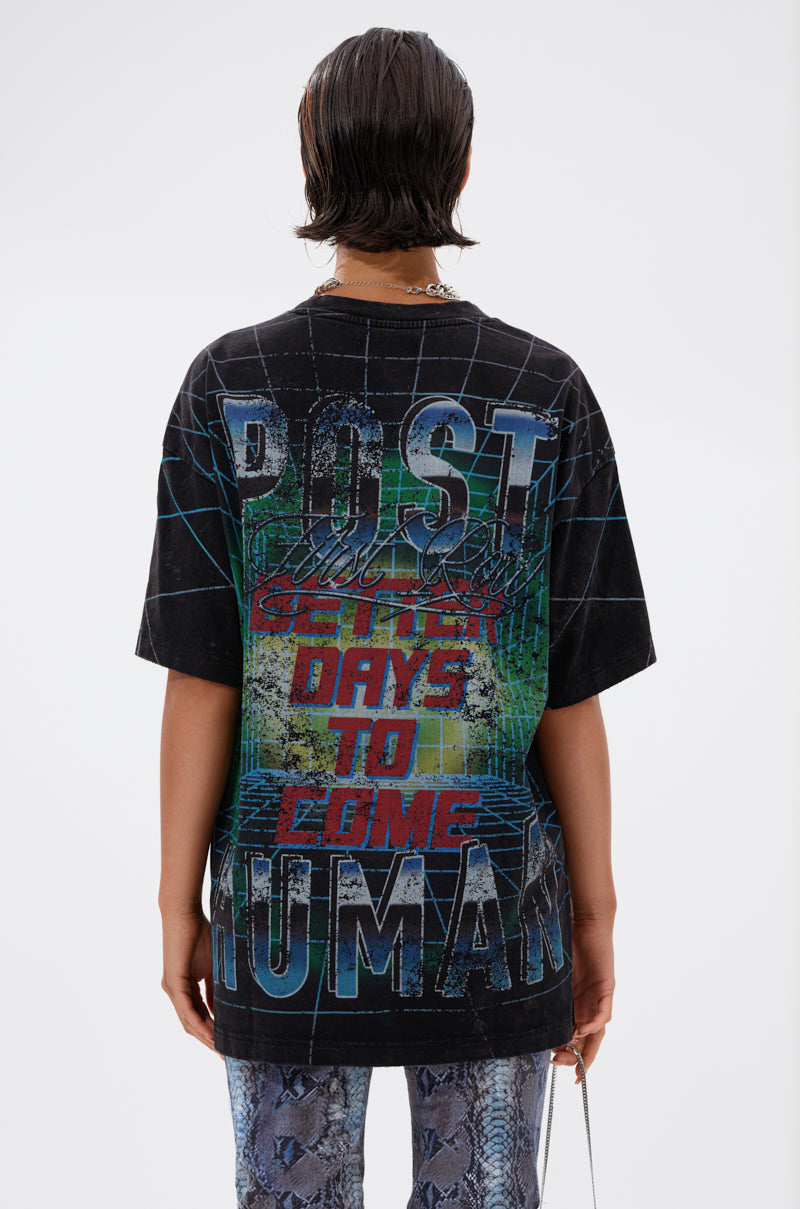 A person with wet, dark hair, facing away, wears the METAVERSE OVERSIZED GRAPHIC TEE featuring bold, colorful "POST HUMAN: BETTER DAYS TO COME" text and pairs it with patterned blue pants against a plain white background.