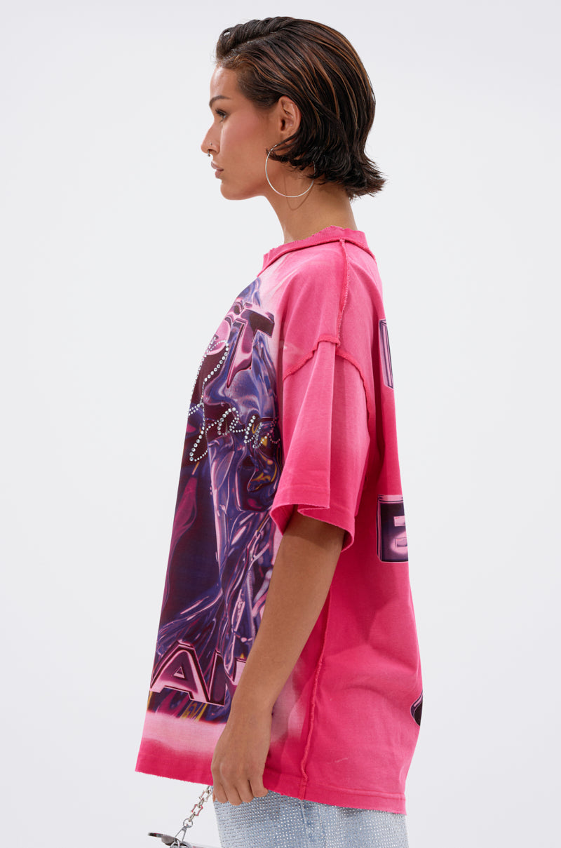 A person with short dark hair and large hoop earrings stands in profile against a plain light background, showcasing the POST HUMAN OVERSIZED GRAPHIC TEE IN PINK for a cool streetwear vibe.