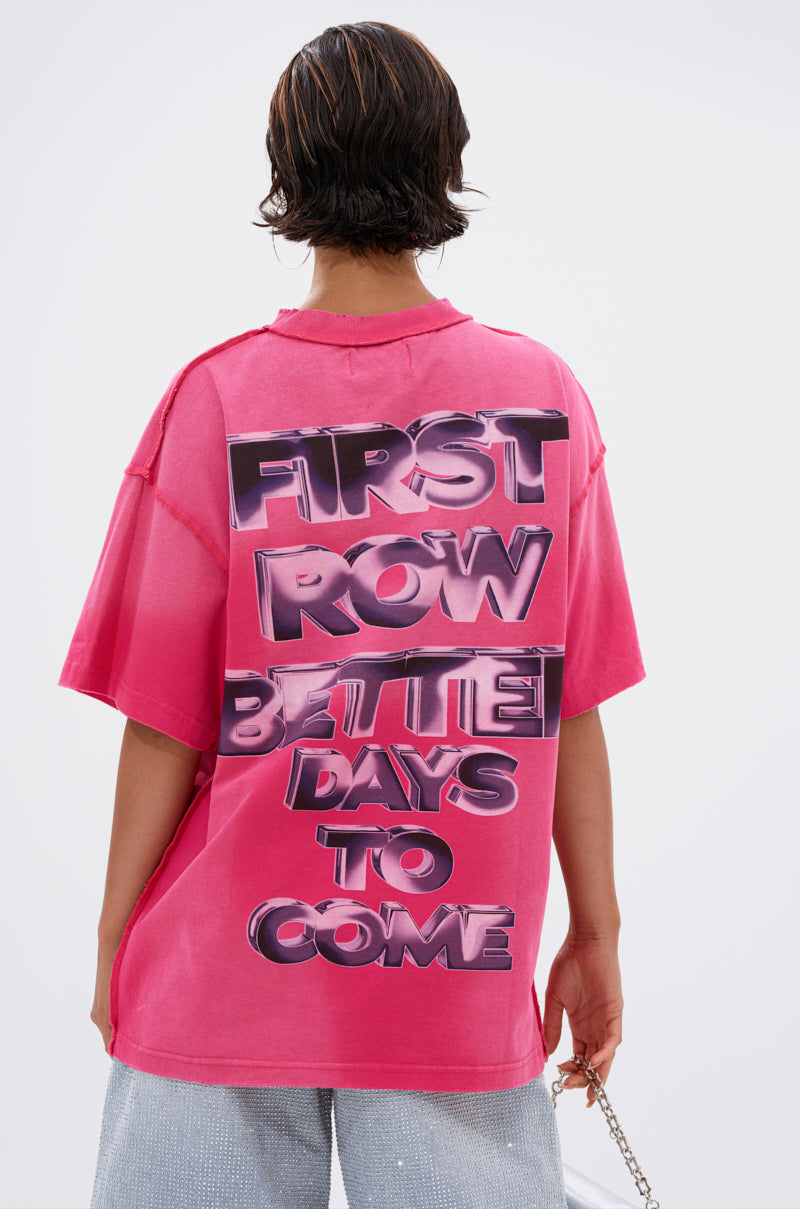 A person with short, dark hair faces away from the camera in the POST HUMAN OVERSIZED GRAPHIC TEE IN PINK, featuring bold metallic "FIRST ROW BETTER DAYS TO COME" text on the back for a cool streetwear look.