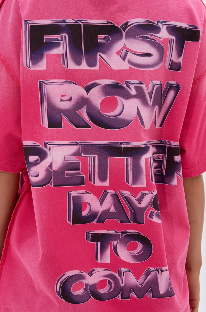 A person wears the POST HUMAN OVERSIZED GRAPHIC TEE IN PINK, featuring large, bold shiny text "FIRST ROW BETTER DAYS TO COME" on the back.