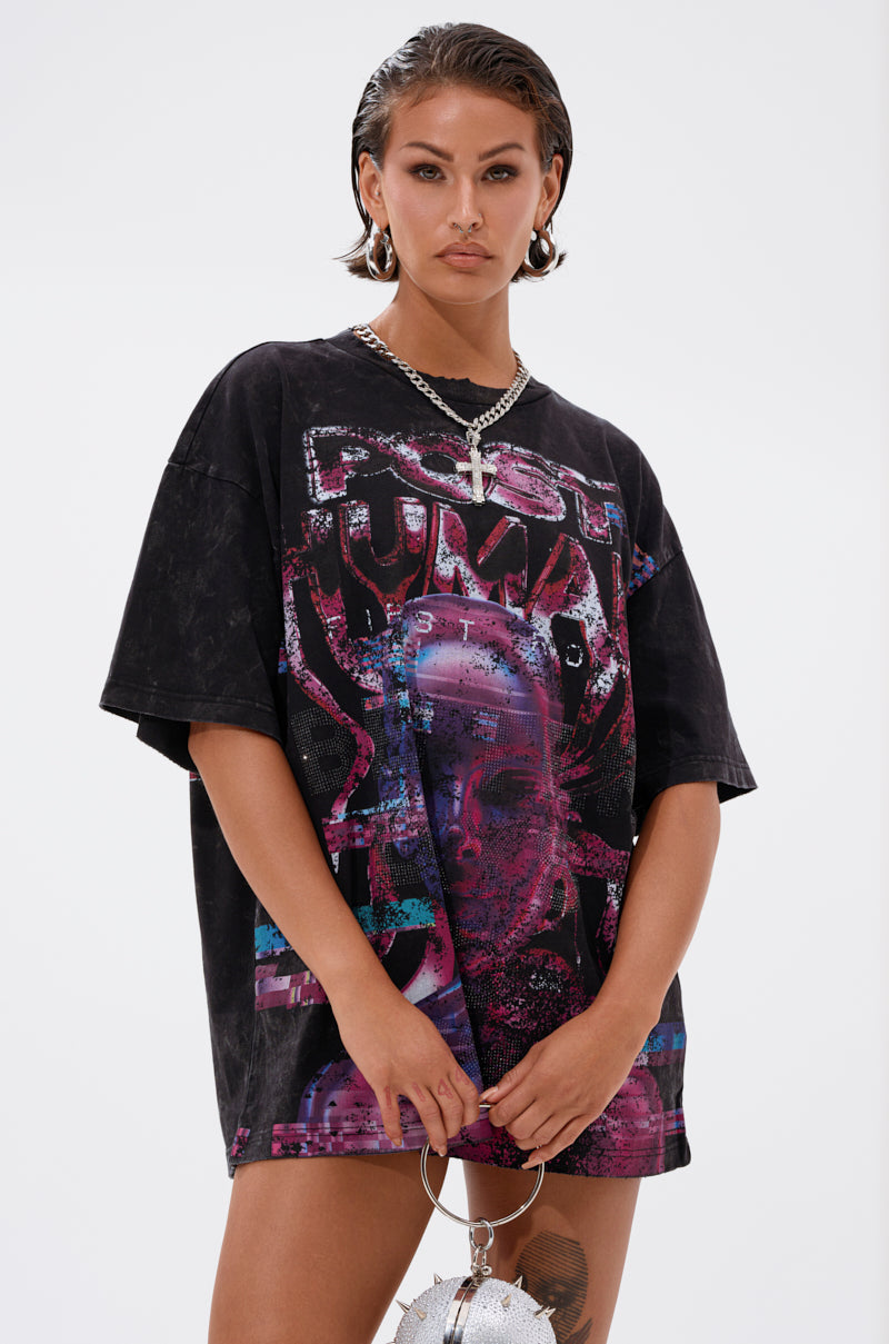 A person with slicked-back hair wears hoop earrings, layered silver necklaces, and the FIRST ROW CYBERTRONICS OVERSIZED GRAPHIC TEE with bold, colorful graphics—embodying futuristic streetwear—posing against a white background holding a small silver bag. 1