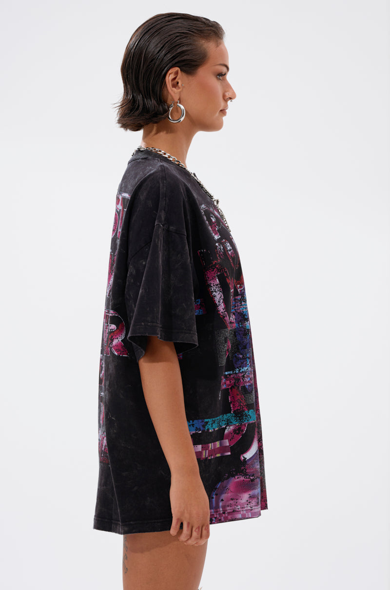 A person with short dark hair and large hoop earrings wears the FIRST ROW CYBERTRONICS OVERSIZED GRAPHIC TEE, featuring colorful designs, while standing in profile against a plain white background. 2