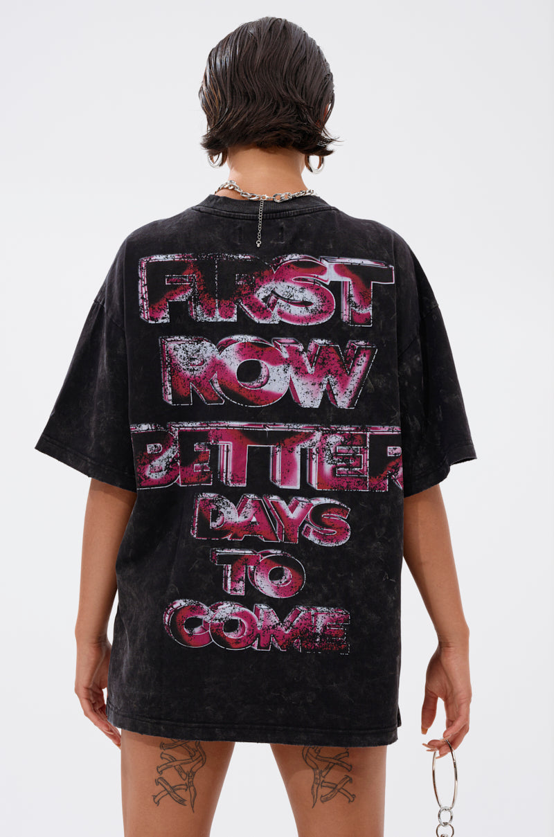 A person with short wet hair faces away, wearing the FIRST ROW CYBERTRONICS OVERSIZED GRAPHIC TEE featuring bold pink and silver "FIRST NOW BETTER DAYS TO COME" text, holding sunglasses for a futuristic streetwear look. 3