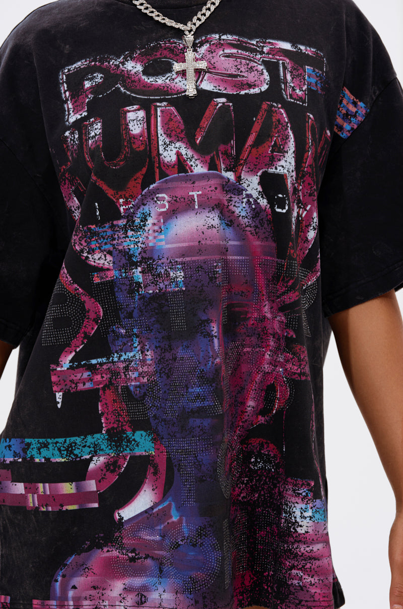 A person wears the FIRST ROW CYBERTRONICS OVERSIZED GRAPHIC TEE, featuring a bold graphic head design and distressed lettering, styled with a silver chain and cross pendant for a standout futuristic streetwear look. 7