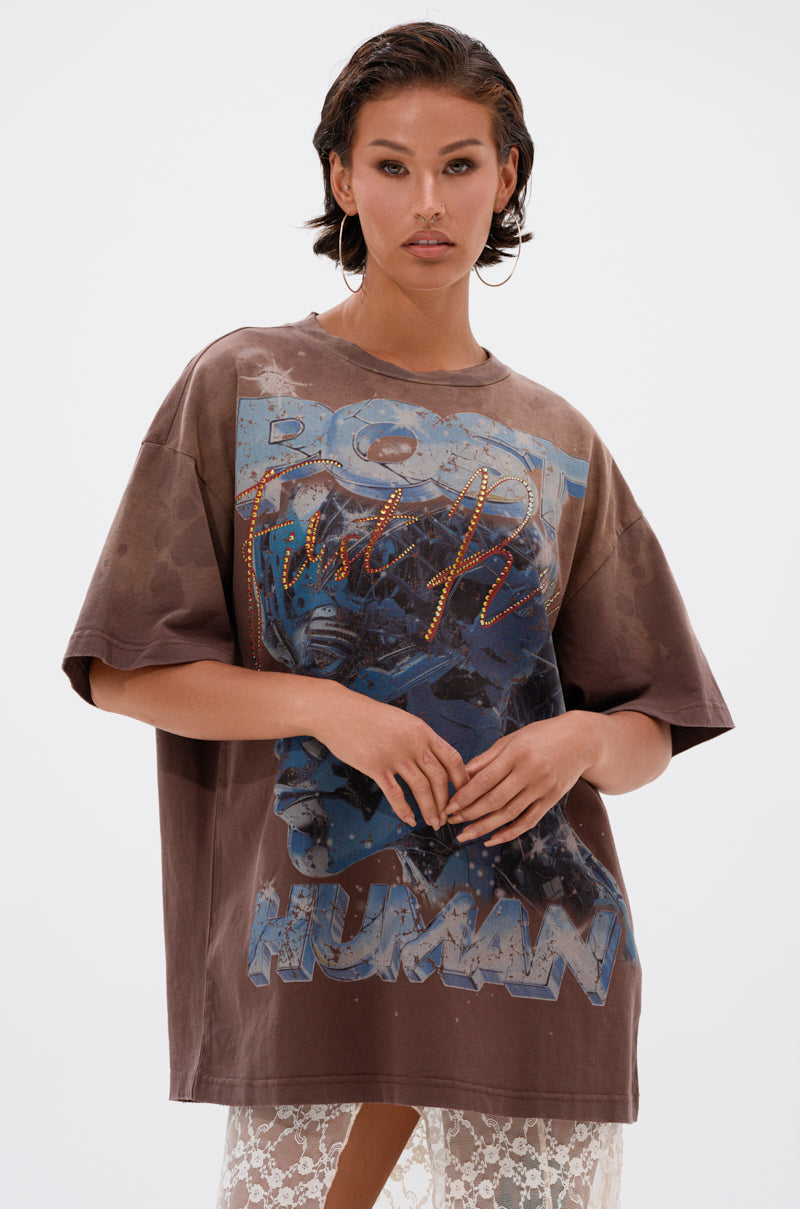 A woman with wet hair models the POST HUMAN OVERSIZED GRAPHIC TEE, a brown streetwear shirt with "HUMAN" and stylized text, paired with a sheer lace skirt against a plain white background. 0