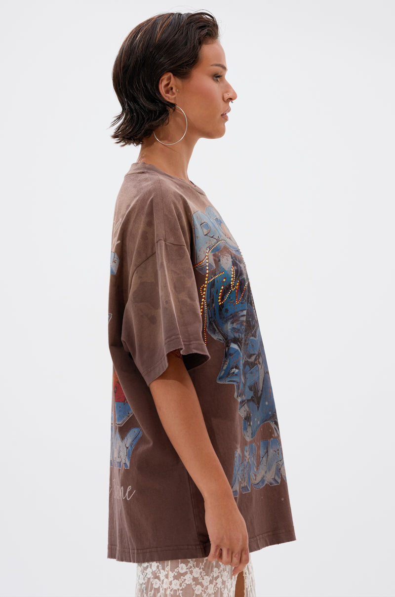 A woman with short dark hair and large hoop earrings stands in profile against a plain white background, wearing the POST HUMAN OVERSIZED GRAPHIC TEE. 2