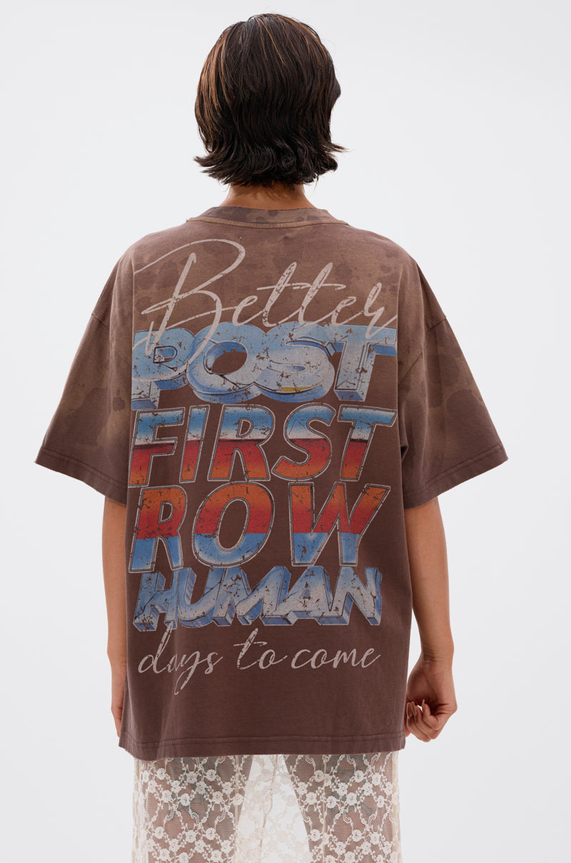 A person with short, dark hair is seen from behind, wearing the POST HUMAN OVERSIZED GRAPHIC TEE with bold, colorful text and pairing it with a long, sheer lace skirt for a cyberpunk streetwear vibe. 3