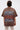 A person with short, dark hair is seen from behind, wearing the POST HUMAN OVERSIZED GRAPHIC TEE with bold, colorful text and pairing it with a long, sheer lace skirt for a cyberpunk streetwear vibe.