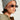 A person wearing a NEUTRAL GREY CLASSIC BEANIE for added warmth, along with sunglasses and an olive green jacket with the zipper partially open. The individual showcases a septum piercing and small hoop earrings, set against a plain, light-colored background.