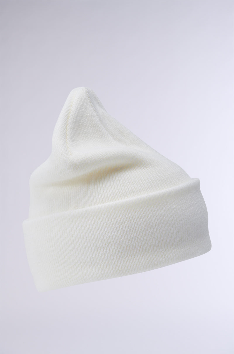 The WINTER WHITE CLASSIC BEANIE, with its cozy knit design and fold-over brim, rests on a light gray background. This beanie is crafted from stretch knit material and showcases a slightly pointed top along with a visible ribbed texture.