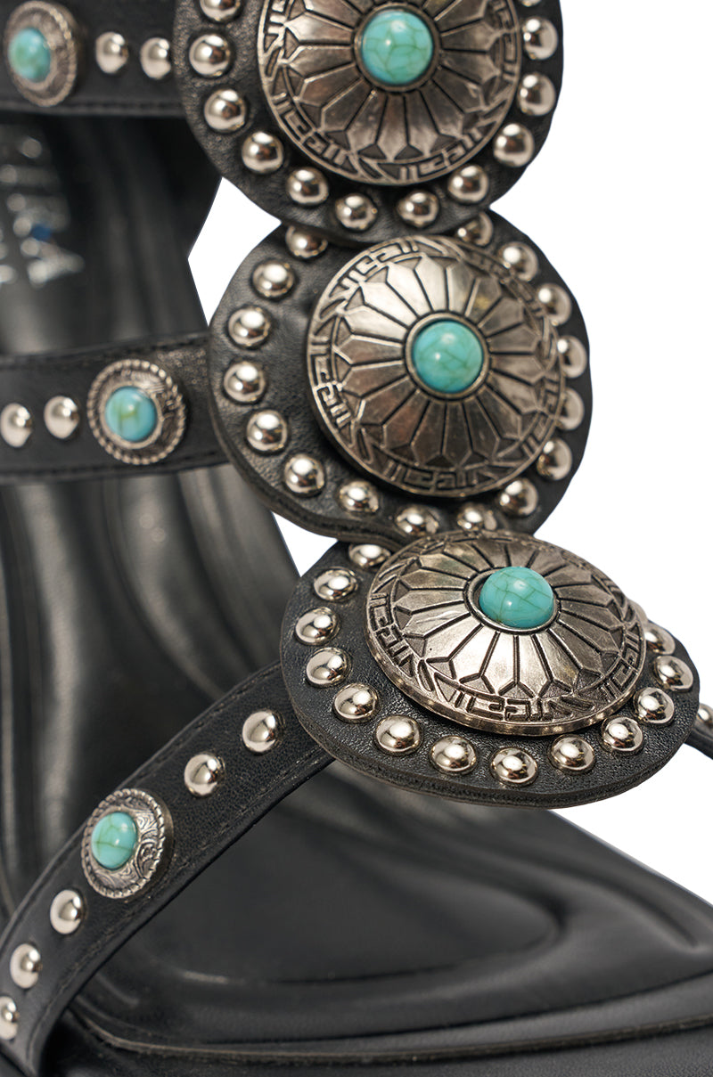 Close-up of the AKIRA GOLD FUANMARA BLACK EMBELLISHED SEXY STILETTO PU SANDAL featuring a black boho-chic design, silver engraved conchos with turquoise stones, and silver studs on the straps. 6