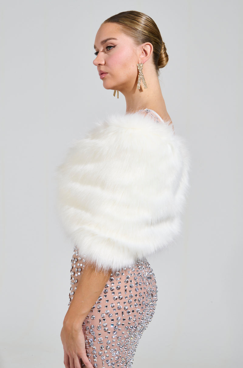 A woman stands in profile, draped in the dazzling TO THE GALA FAUX FUR SHAWL over a glamorous, gem-studded high-glam gown. Her hair is elegantly styled in an updo, and she wears long drop earrings, exuding sophistication and elegance. 4