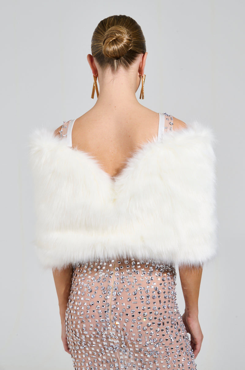 With her back to the camera, a woman radiates elegance in a high-glam gown, enhanced by the "TO THE GALA FAUX FUR SHAWL" in white. Her hair is styled into a sleek bun, and she showcases long earrings against a simple, light-colored background. 5