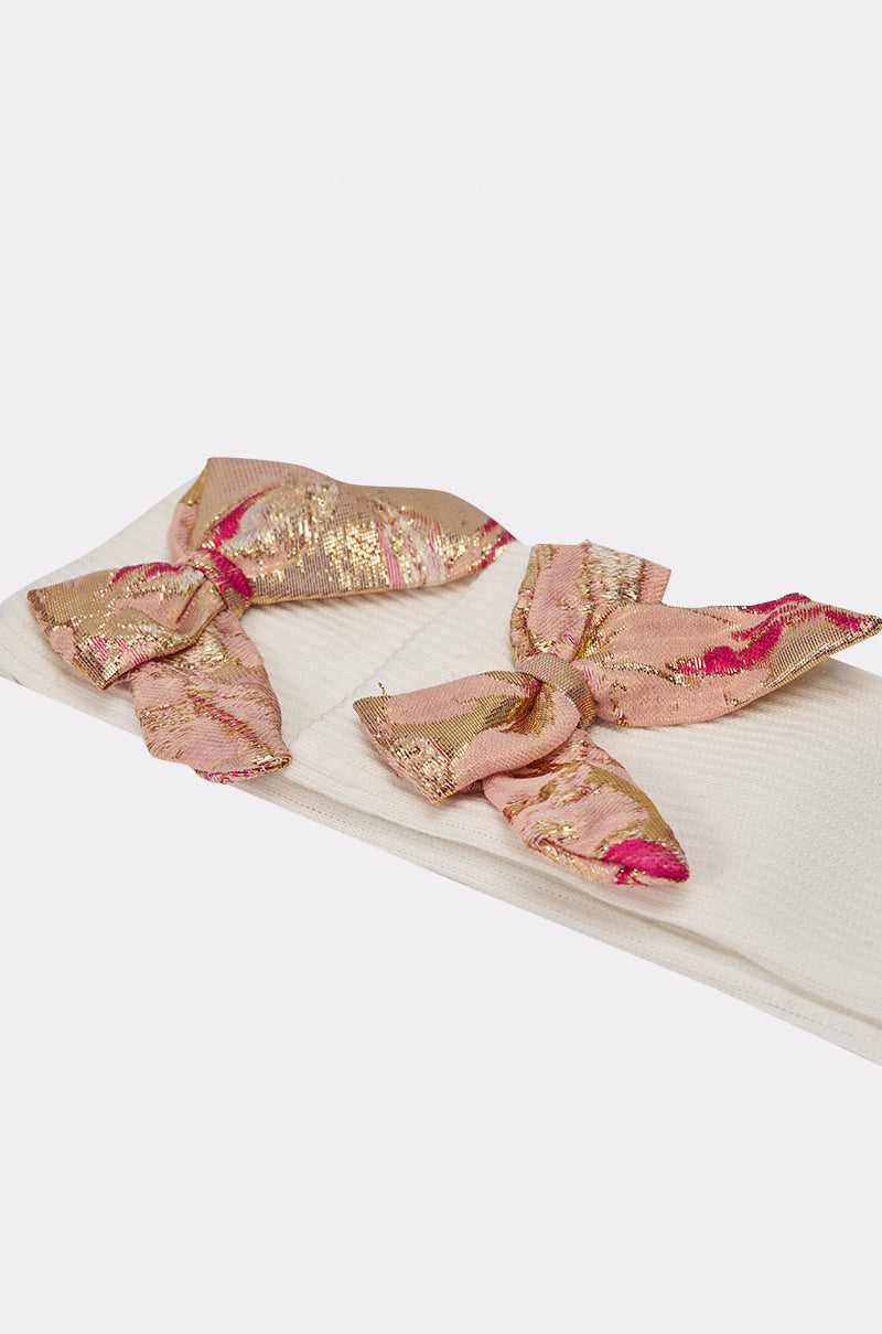 The DOLLED UP BOW SOCKS are ivory textured knee-highs adorned with large pink and gold brocade bows near the cuff. 4