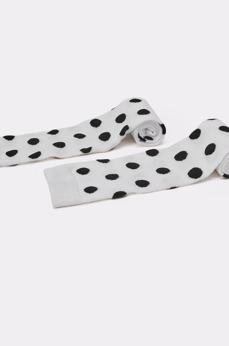 The CALL ME DOTTIE KNEE HIGH SOCKS are playful white knee-high socks with bold black polka dots, shown flat on a light background with the toes rolled inward. 4