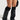 The individual sporting tall black leather boots with stiletto heels and LAYERED UP LEGWARMERS exudes a cozy vibe while wearing a snakeskin-patterned mini skirt. In their left hand, they hold a bag against a neutral background.