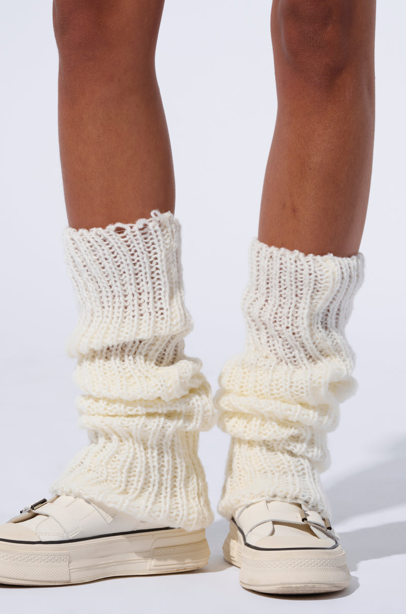 Close-up of a person wearing LAYERED UP LEGWARMERS in off-white, slouched around the calves, paired with white platform sneakers featuring a buckle detail. The backdrop is white, highlighting the footwear and balletcore accessories.