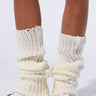 Close-up of a person wearing LAYERED UP LEGWARMERS in off-white, slouched around the calves, paired with white platform sneakers featuring a buckle detail. The backdrop is white, highlighting the footwear and balletcore accessories.