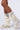 A person is wearing LAYERED UP LEGWARMERS in a chunky knit style, scrunched down over bare legs, paired with cream-colored loafers featuring a buckle detail. The plain white background emphasizes the cozy, stylish look of these balletcore accessories and shoes.