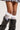 Close-up of a person wearing RUFFLE MANIA KNEE HIGH SOCKS with ribbon accents, paired with black leather boots featuring buckle details. The individual also sports a pleated skirt that partially appears at the top of the image.